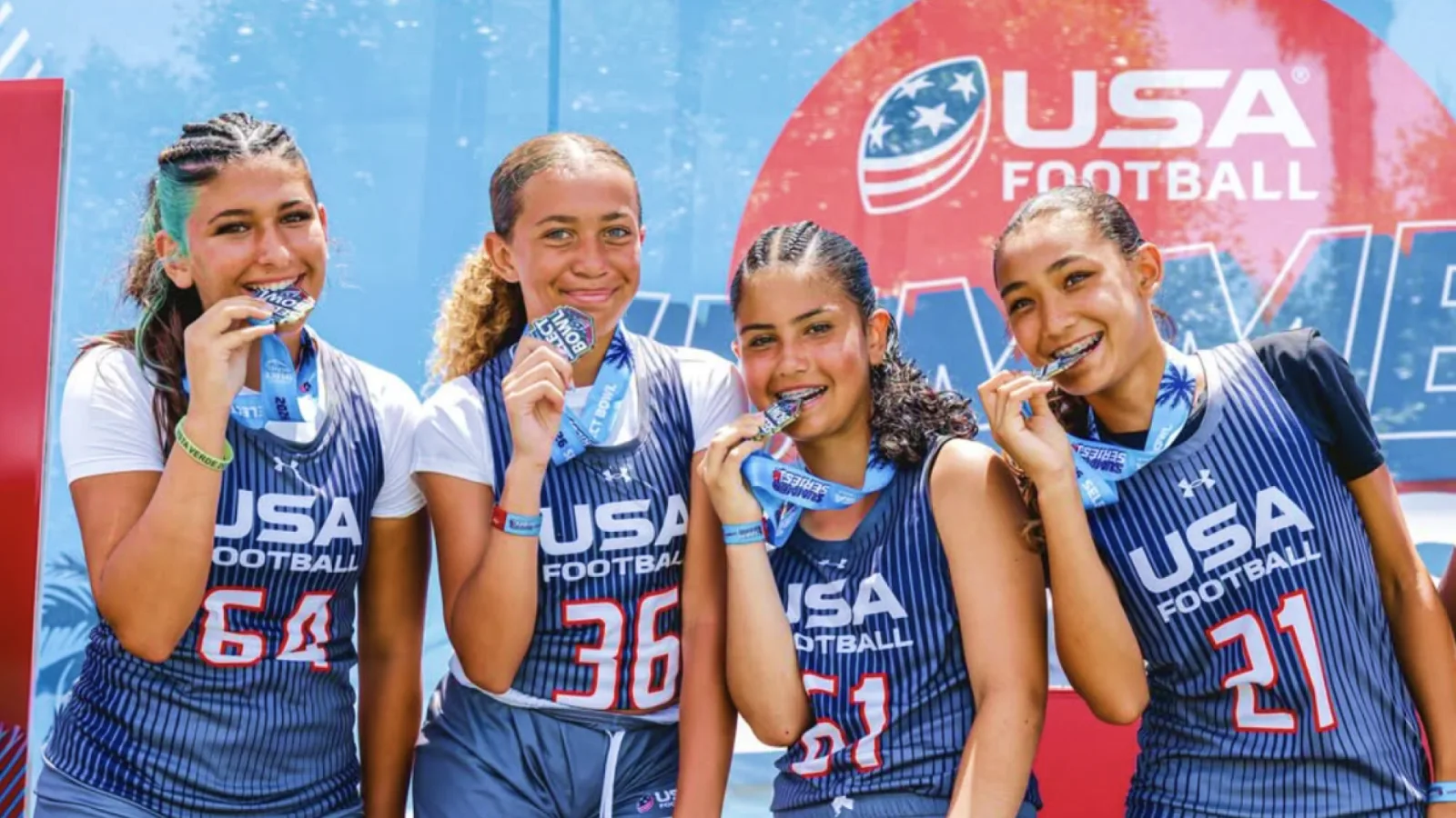Four athletes biting their Select Bowl medals in front of the USA Football backdrop